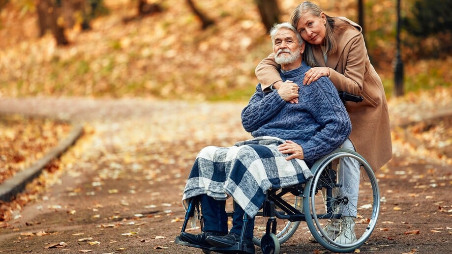 Betreuungswelt-Friesch Senior sitzt im Rollstuhl, begleitet von einer Angehörigen; beide genießen die Zeit im herbstlichen Park