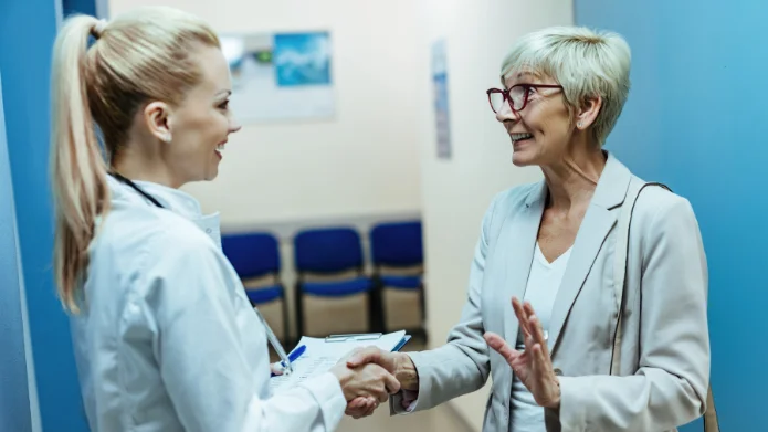 Ärztin und Patientin (60+) besprechen Vorsorgeuntersuchungen wie Darmspiegelung und Mammographie-Screening in einer Praxis.