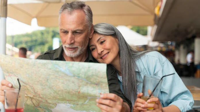 Ein Paar im fortgeschrittenen Alter sitzt an einem Tisch im Freien und betrachtet gemeinsam eine Landkarte.