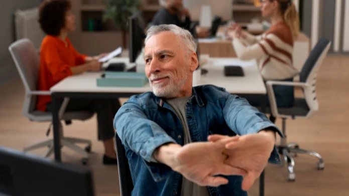 Aktivrente 2026: Bis zu 2.000 € steuerfrei im Rentenalter Mann im Rentenalter arbeitet in einem Büro und dehnt sich am Schreibtisch während des Arbeitstags.