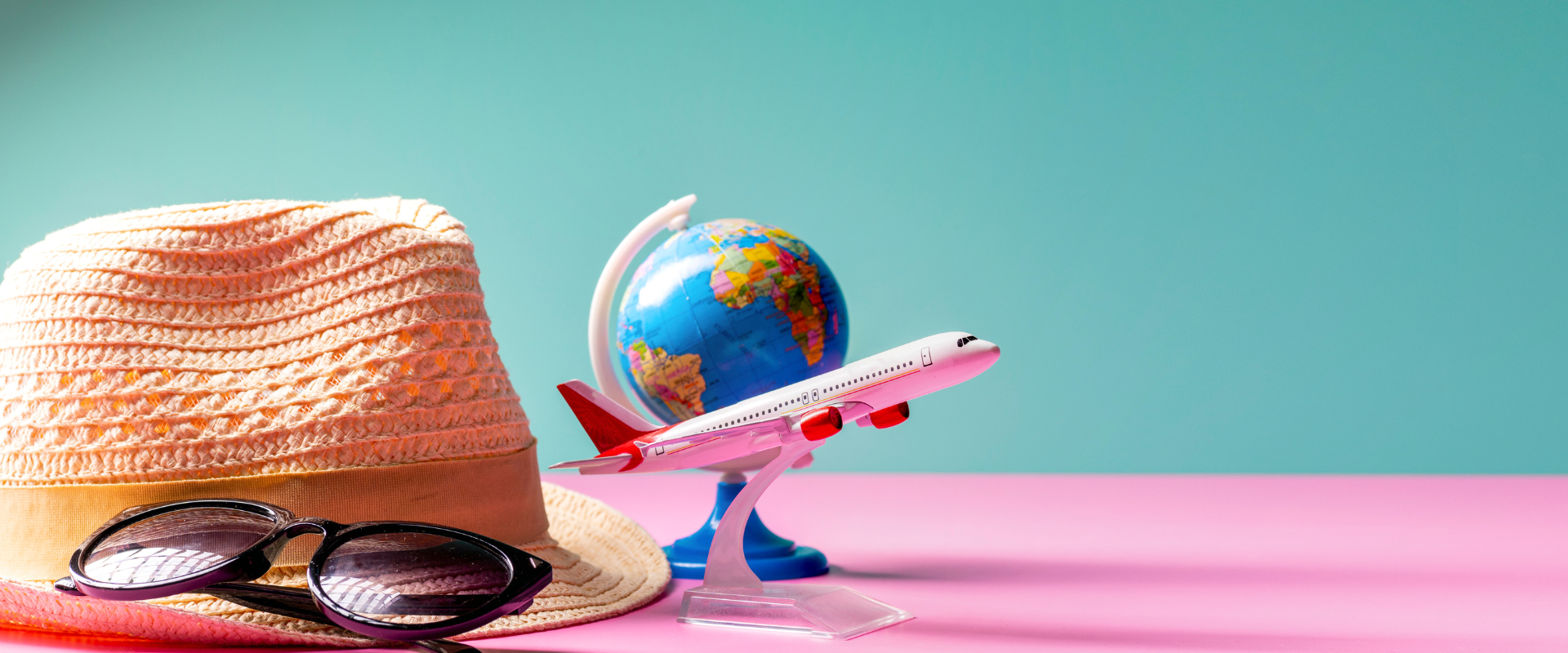 Reisebüros Ein Strohhut, eine Sonnenbrille, ein Modellflugzeug und ein Globus stehen vor farbigem Hintergrund als Symbole für Reisen und Urlaubsplanung.