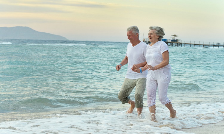 Älteres Paar läuft den Strand entlang. Im Hintergrund das Meer und ein atemberaubender Sonnenuntergang. 