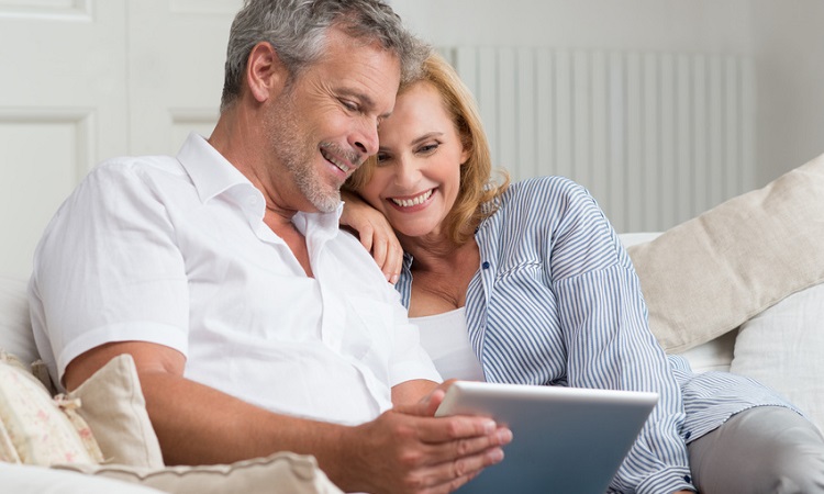 Älteres Paar sitzt mit einem Tablet auf dem Sofa und surft im Internet. 