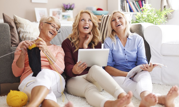 Mutter, Tochter und Oma sitzen auf dem Fußboden und haben Spaß beim Online-Shopping über ein Tablet. 