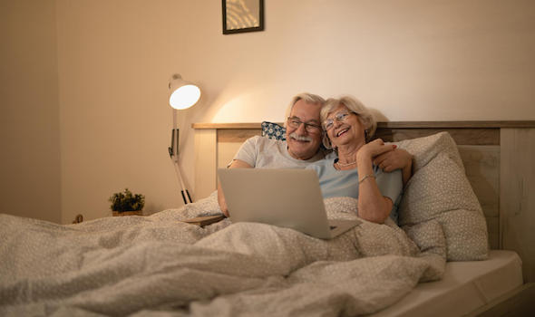 happy-senior-couple-lying-down-in-bed-and-surfing-the-net-on-laptop-at-night.jpeg
